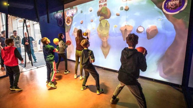 Children playing a projected video game by throwing balls at a wall