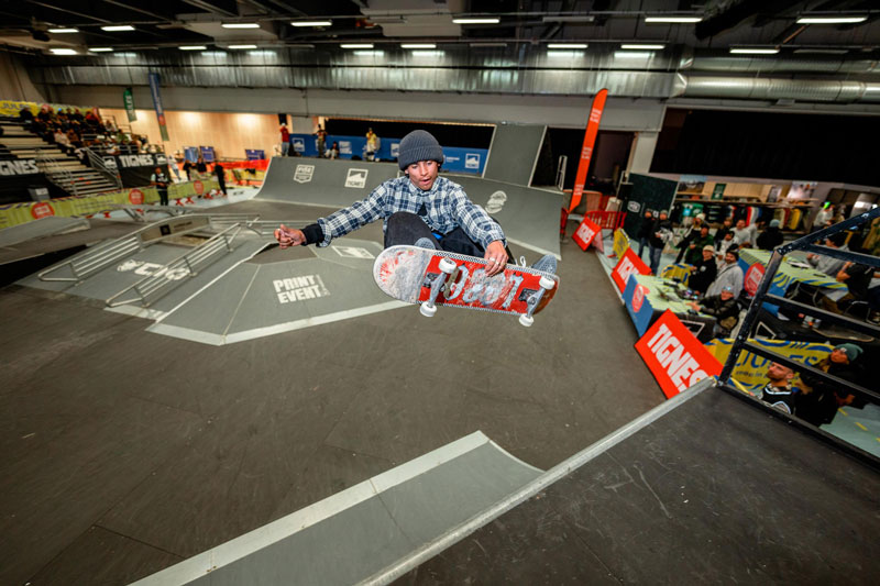 Freeze frame of a youngster doing tricks with a red skateboard in a skatepark at Paris Games Week. 