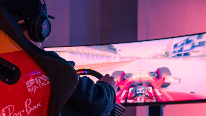 Photo of a man from behind playing a car racing game on a racing simulator