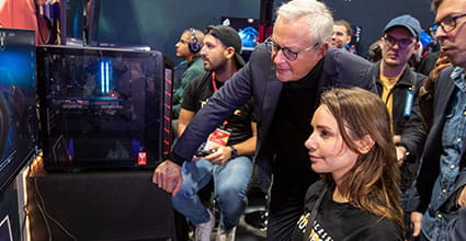 Seated woman playing a video game surrounded by a group watching her play