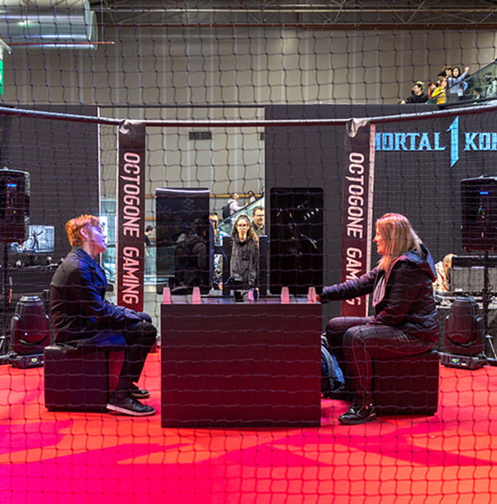 deux personnes discutant dans une arène sur le stand de Mortal Kombat à la Paris Games Week